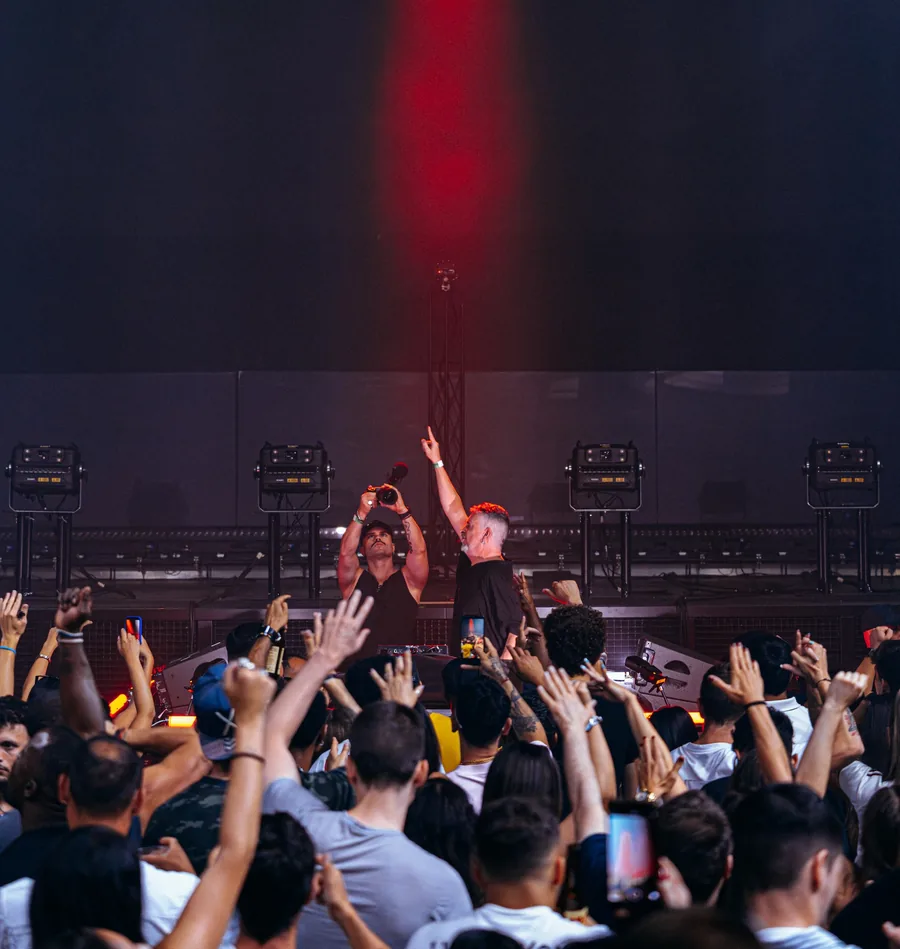 DJ INO on stage with the crowd&rsquo;s hands up under a red light beam